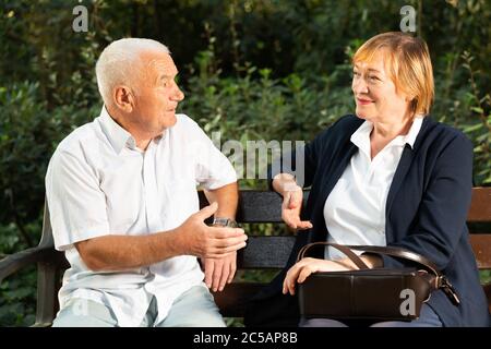 Una coppia anziana che parla emotivamente seduto in panchina nel parco il giorno di sole Foto Stock