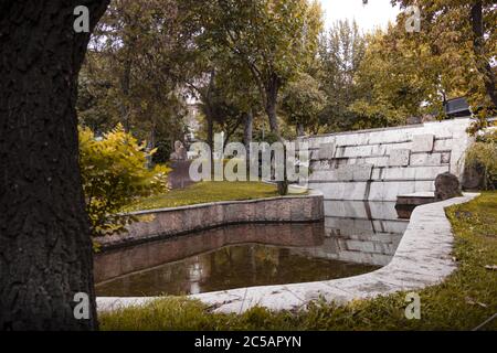 Parco con laghetto circondato da alberi e un muro di mattoni Foto Stock