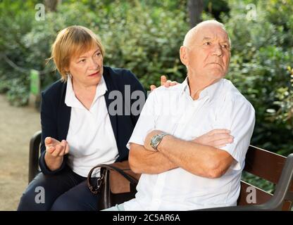 Uomo anziano seduto si è allontanato da anziana scusante donna sulla panchina nel parco Foto Stock