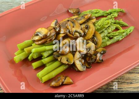 Asparagi freschi cotti con salsa di funghi su piatto di portata rosso Foto Stock