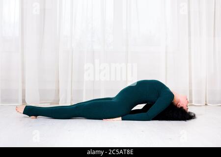 ragazza in abbigliamento sportivo facendo esercizi di yoga con arching della schiena nella stanza durante gli sport di lavoro di quarantena sdraiati sul pavimento. Foto Stock