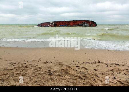 spiaggia di sabbia in tempo nuvoloso in mare con onde in acqua sul suo lato si trova una nave rovesciata naufragata dopo una tempesta. Foto Stock