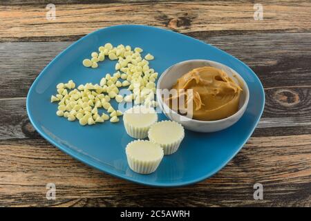 Tazze di burro di arachidi al cioccolato bianco su piatto blu con scaglie di cioccolato bianco e burro di arachidi in recipiente grigio Foto Stock