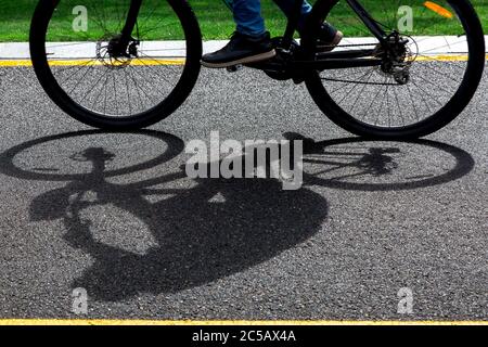 pista da bici asfaltata con marcature gialle con una bici nera che passa sfocata in movimento durante il giorno di sole estivo, sfondo sportivo su un tema di bicicletta da vicino. Foto Stock