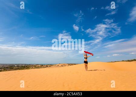 Bella ragazza caucasica che si diverte sulle dune di sabbia rossa a Mui NE, Phan Tiet zona in Vietnam. Paesaggio con cielo blu durante la giornata di sole. Foto Stock