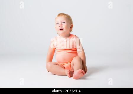 La bambina bionda ride in un bodysuit arancione seduto su sfondo bianco Foto Stock