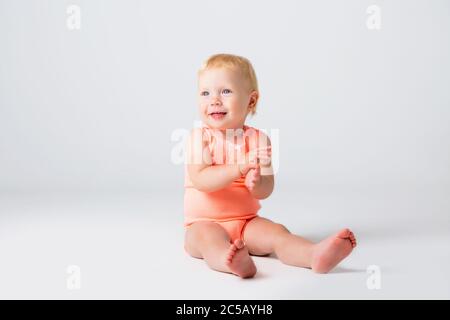 La bambina bionda ride in un bodysuit arancione seduto su sfondo bianco Foto Stock