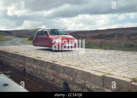 Surreale che sorpassa Ford Ka su un ponte di pietra sulle brughiere di york del nord, Yorkshire Foto Stock