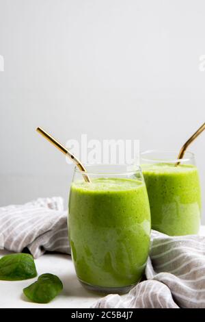 Green Smoothie servito in un bicchiere con una paglia e spinaci su marmo Foto Stock