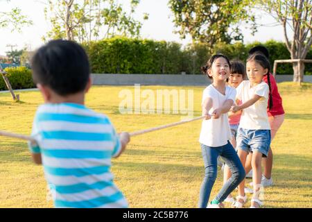 Gruppo di bambini asiatici giovani felici che giocano un rimorchiatore di guerra o tirano la corda all'esterno nel parco giochi della città nel giorno d'estate. Bambini e ricreazione c Foto Stock