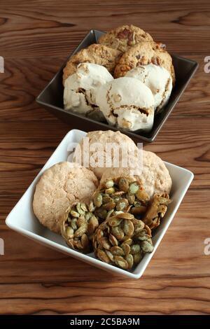 Biscotti di farinata d'avena con noci e uvetta, biscotti di semi di zucca ricoperti di zucchero, biscotti di meringa con nocciole, biscotti di mandorle in una ciotola quadrata su un wo Foto Stock