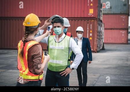 Coronavirus Covid-19 malattia situazione di crisi epidemica, contenitore che spediscono lavoratore avente febbre corpo scansione da termometro scansione a nave Yard. Corona- Foto Stock