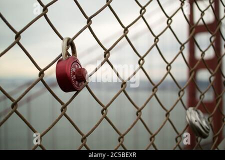 Lucchetti d'amore sul Golden Gate Bridge, San Francisco, California. Lucchetto rosso e lucchetto rotondo. Torre nord di ponte iconico sullo sfondo. Foto Stock