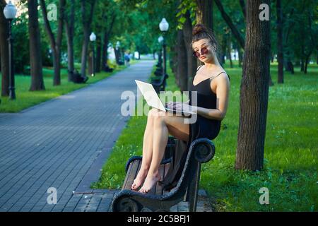 bella ragazza cammina per la città, lavorando su un computer portatile, tenendo un computer portatile e ascoltando musica. Foto Stock