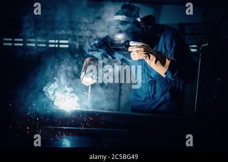 Il saldatore tecnico lavora la saldatura dell'acciaio in officina di assemblaggio, la struttura saldatrice in attrezzatura di sicurezza è la saldatura del metallo nella produzione di assemblaggio in fabbrica Foto Stock