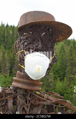 Una statua di metallo, costruita in pezzi di metallo di scarto saldati insieme e qualcosa come bulloni, indossa una maschera protettiva per ricordare alla gente di indossare una du Foto Stock