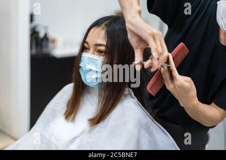 parrucchiere tagliando i capelli ad una cliente femminile, la gente deve essere wering maschera medica per protezione coronavirus (covid-19) pandemic. nuovi concetti normali Foto Stock