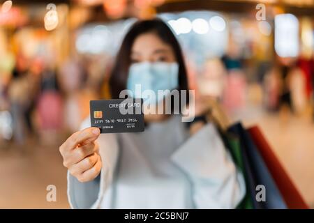 Carta di credito con giovane donna che indossa una maschera medica al centro commerciale per la prevenzione da coronavirus (Covid-19) pandemia. Nuovi concetti normali Foto Stock