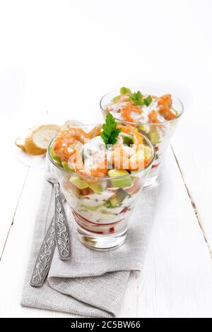 Pasta con insalata di gamberetti, avocado, Fresco cetriolo e peperone e pomodoro condito con salsa di yogurt in due bicchieri di vetro su un asciugamano, pane e delle forcelle Foto Stock