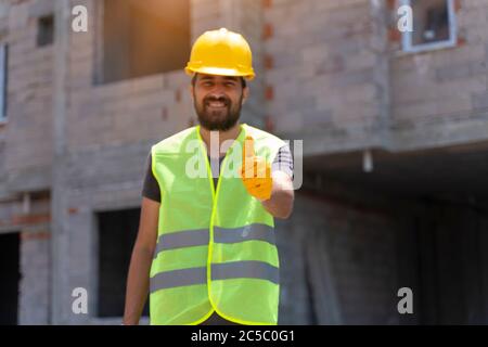 Lavoratore in un cantiere con pollici in su e sorridente. Influenza lavoratore background Foto Stock