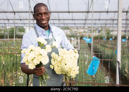 Uomo afroamericano con bouquet di fiori freschi di garofano in serra Foto Stock