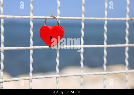 Lucchetto rosso cuore sulla recinzione di fronte al mare blu, simbolo di amore eterno Foto Stock