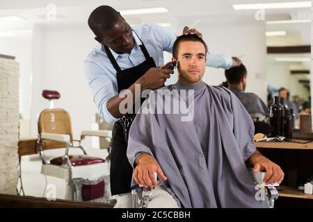 Giovane uomo di ottenere il taglio dei capelli con electric clipper professionale barbiere africani in salone Foto Stock