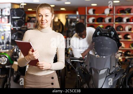 Venditore femminile adulto che tiene la brochure pubblicitaria nel salone moderno del motociclo Foto Stock