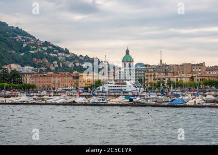 Vista del porto della città di Como. Numerosi yacht ancorati e una grande nave da crociera, gli antichi edifici colorati e la cupola della cattedrale sopra di loro. Foto Stock