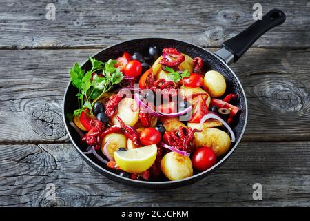 Insalata di polpo con patate giovani, olio d'oliva, succo di limone, pomodori ciliegini, fette di cipolla rossa, olive nere, prezzemolo su una padella di legno Foto Stock