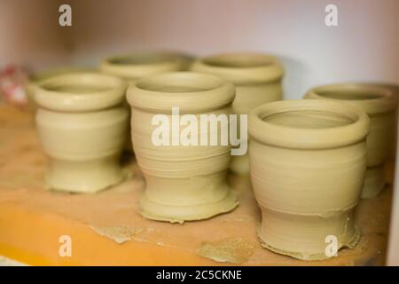 Tazze incompiite in fila su scaffale di laboratorio di ceramica, studio di ceramica - vista ravvicinata. Artigianato, fai da te, arte e concept fatto a mano Foto Stock