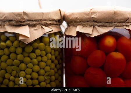 primo piano con gustosi pomodori in scatola fatti in casa e piselli verdi in vasi Foto Stock