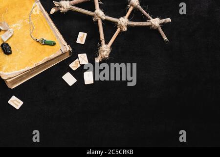 vista dall'alto delle rune vicino al pentagramma, cristalli e libro vecchio sul nero Foto Stock