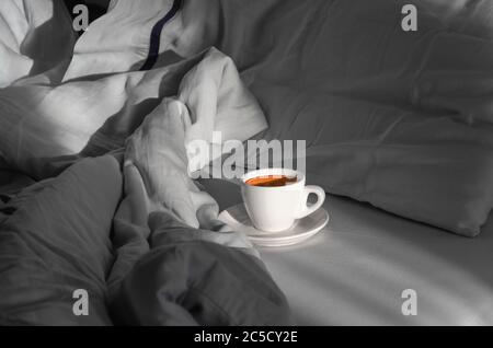 Caffè mattutino a letto. Tazza di caffè sul letto in camera con molta luce naturale. Concetto di mattina. Godendo le piccole cose Foto Stock