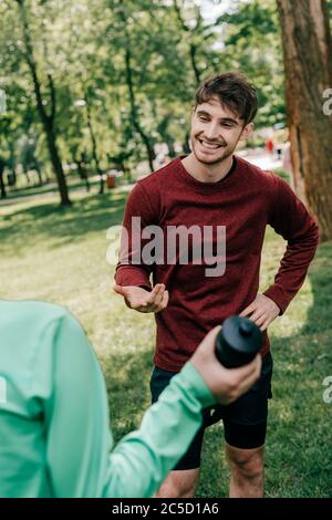 Fuoco selettivo di un bel sportivo che parla con la ragazza con una bottiglia sportiva nel parco Foto Stock