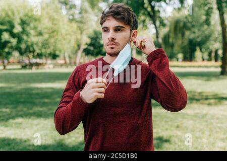 Bel sportivo che prende la maschera medica nel parco Foto Stock