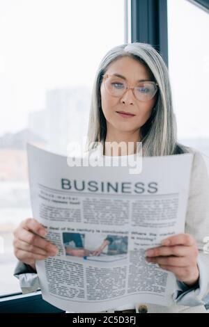 fiducioso donna d'affari asiatica che legge giornale di affari in ufficio Foto Stock