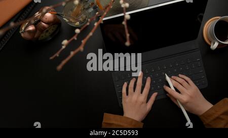 Foto a testa di mano femminile che scriva sulla tastiera digitale del tablet su una scrivania da ufficio di lusso scura con decorazioni Foto Stock