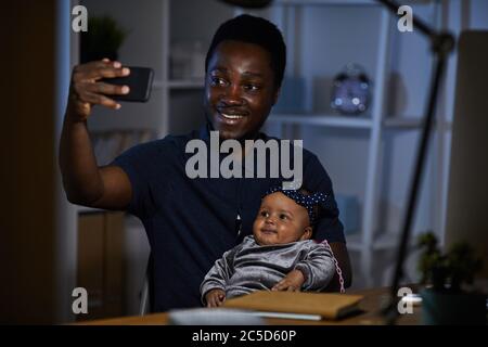 African felice padre che fa selfie con la sua figlia del bambino sul telefono mobile mentre sedevano al tavolo Foto Stock