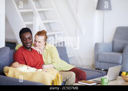 I giovani genitori seduti sul divano e guardando il loro bambino mentre dormiva si siedono sul divano nel soggiorno Foto Stock