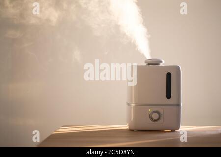 Primo piano del diffusore di olio aromatico sul tavolo a casa, vapore dall'umidificatore dell'aria, spazio di copia. Tecnologia a ultrasuoni, aumento dell'umidità dell'aria in ambienti interni Foto Stock