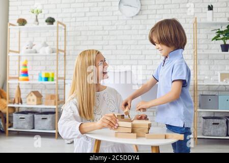 Bella giovane madre che gioca a tavola con suo figlio a casa. Casa madre e bambino torre di costruzione da blocchi di legno Foto Stock