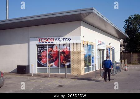 La donna acquirente emerge dal negozio Tesco express in Cornelly del Nord indossando una maschera durante la pandemia del coronavirus 2020 Foto Stock