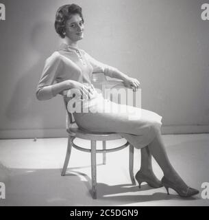 Fine degli anni '1940, storica, una elegante e graziosa giovane donna inglese, metà-fine anni '20 in uno studio di fronte a uno schermo seduto su una sedia a bottone di legno che modellava le ultime mode femminili, un abito in due pezzi con top e gonna di lana, Inghilterra, Regno Unito. In quest'epoca, l'aspetto austerità degli anni della guerra fu sostituito dalla femminilità di un look più morbido, spalle strette, vita aderente, busto enfatizzato e gonne più lunghe, con l'influenza di stilisti parigini come Christian Dior. Foto Stock