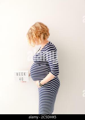 Giovane donna caucasica incinta che tocca la ventre in crescita e tiene un segno con 40 settimane Foto Stock