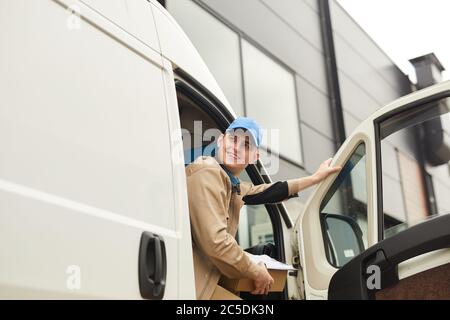 Giovane sorridente corriere che tiene il pacchetto mentre si siede nel furgone che consegna pacchi Foto Stock
