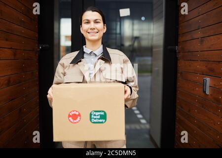 Ritratto di giovane donna sorridente alla macchina fotografica mentre tiene il pacco che consegna il cibo da asporto Foto Stock