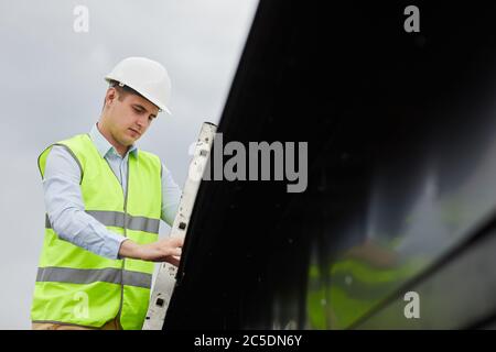 Uomo in casco da lavoro e in giubbotto che lavora all'aperto nel cantiere Foto Stock