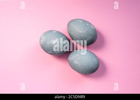 Uova di pasqua di colore grigio su sfondo rosa. Tre uova tinte a colori di cemento. Vista dall'alto. Disposizione piatta. Buon concetto di Pasqua Foto Stock