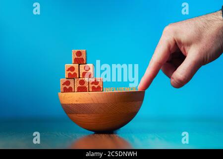 Concetto di business di gestione delle risorse umane e di reclutamento. La mano punta alla fondazione traballante della piramide. Spazio di copia. Sfondo blu. Foto Stock